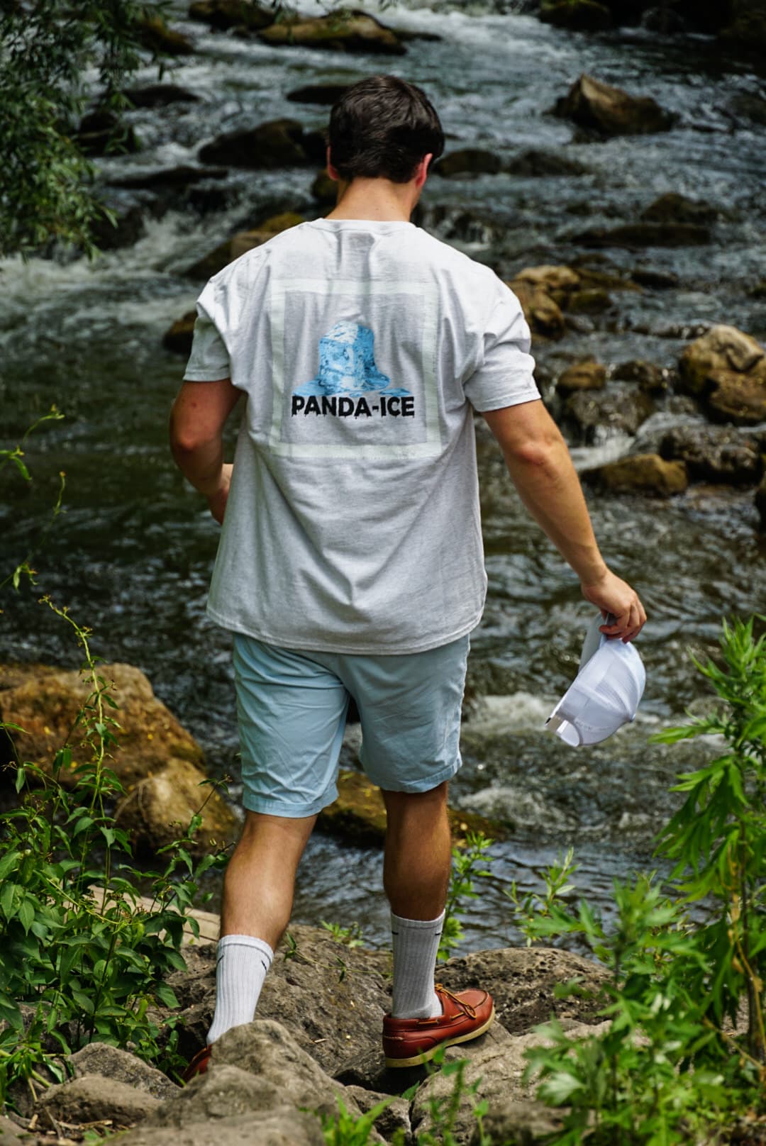 Model wearing a Panda-Ice graphic t-shirt walking over creek rocks during a clothing brand launch shoot