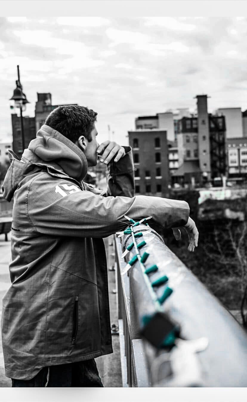 Black and white urban portrait of a man in a rain jacket leaning on a railing above a city skyline